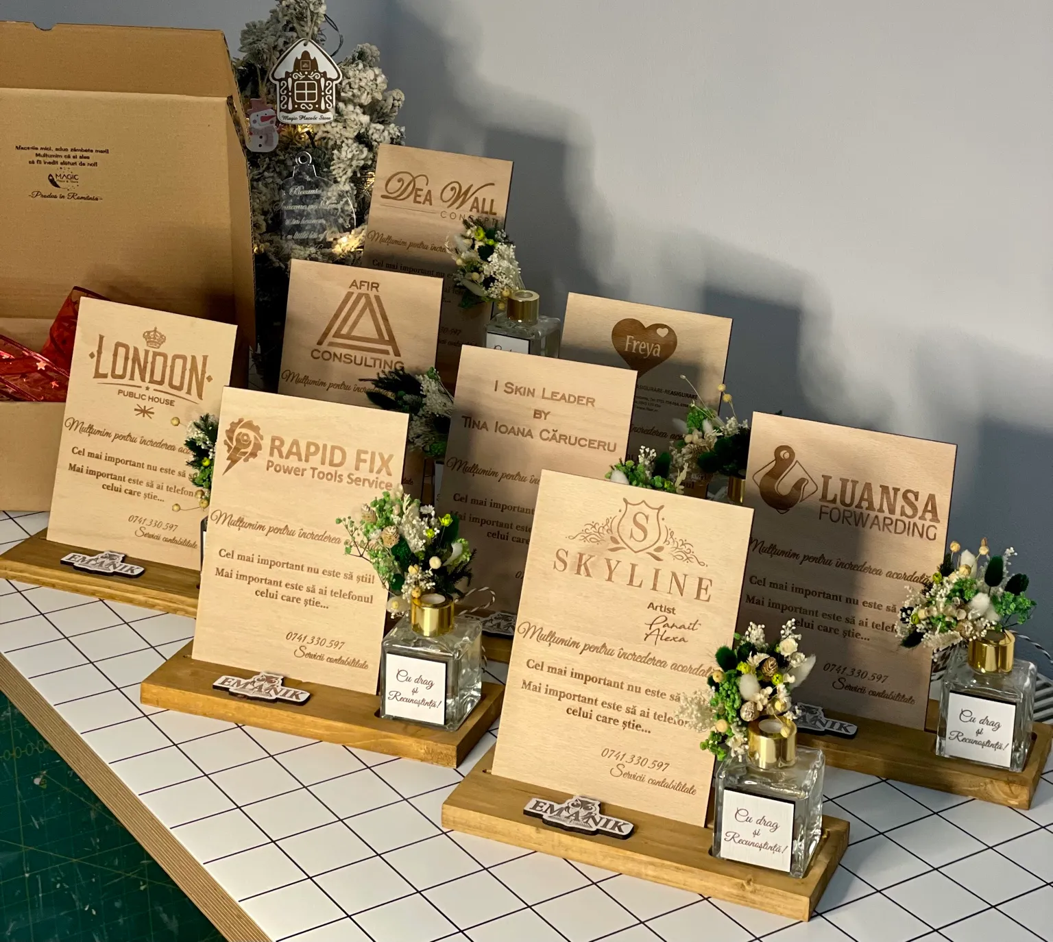 Plachete din lemn cu mesaje de mulțumire și logo-uri de companii, pe suporturi cu decorațiuni florale